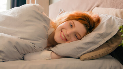 Sleepy beautiful woman waking up lying in comfortable white bed smiling toothy happy smile carefree attractive girl female early good morning relax in cozy bedroom lazy lady awake after sleep at home