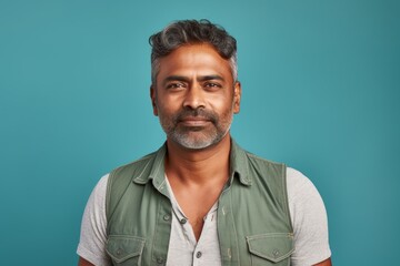 Fototapeta premium Portrait of a glad indian man in his 40s wearing a rugged jean vest in pastel teal background
