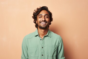 Fototapeta premium Portrait of a blissful indian man in his 20s sporting a breathable hiking shirt in front of pastel brown background