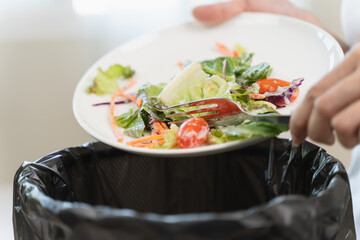 Compost from leftover food in the meal in household, female hand holding left over meal use fork scraping waste, rotten vegetable throwing away into garbage, trash or bin. Environmentally responsible