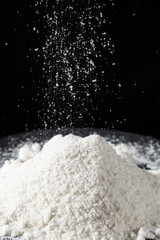 Coconut flour spilling on pile, natural coconut flour texture on black background.