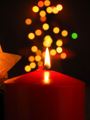 Burning red Advent candle with blurred Christmas lights
