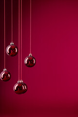 Minimalistic  burgundy Christmas background with hanging ornaments. Christmas decorations featuring crimson and wine-colored ornaments on a deep red background with copy space.