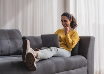 Obraz premium Business woman latin american one person smile happy enjoy sit on sofa and hand holding notebook laptop plan job work new project along with looking success future in living room home office company.