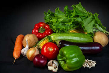A vibrant assortment of fresh organic vegetables, including lettuce, tomato, pepper, garlic, and zucchini, displayed on a black background, symbolizing healthy eating and natural produce.