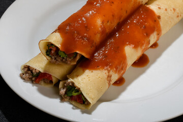 Meat pancake on a white plate with red sauce, dark background