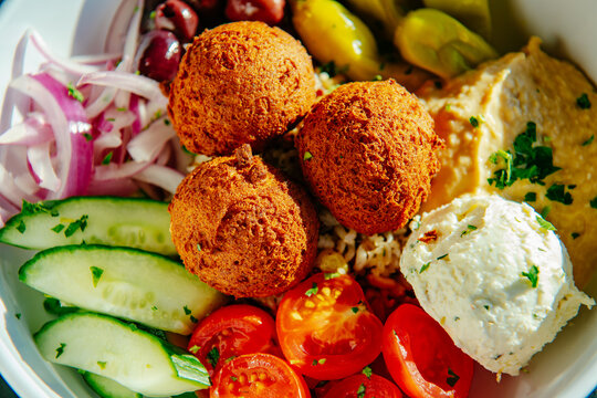 Close up of a Mediterranean bowl with falafel, feta cheese, tomatoes and colorful vegetables