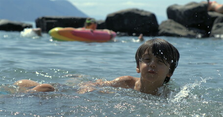Child swimming in lake, water splashing in slow-motion at 800 fps, joyful summer day, rocks in...