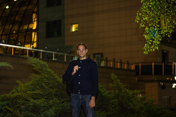 A guy stands against the background of a modern building	

