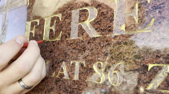 Renovation of golden letters text on a grave with some gold paint and brush