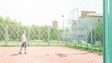 Active young male playing street basketball, dribbling ball, training on court