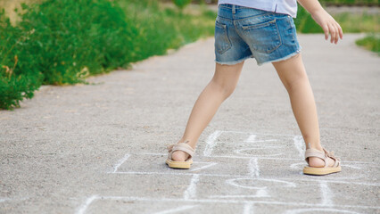 A cute girl is playing hopscotch on the asphalt. Active leisure for children. The concept of a happy childhood.