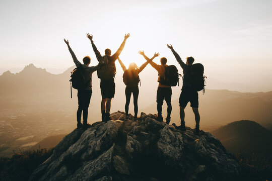Group of friends hiking to a mountain summit, arms raised in triumph as they reach the top together. .