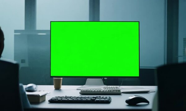 Black flat-screen monitor on a wooden desk, surrounded by a keyboard, mouse, and other computer peripherals in a modern office setting