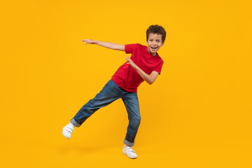 Studio portrait of cute joyfull casually dressed African American schoolboy dancing over bright colored orange yellow background