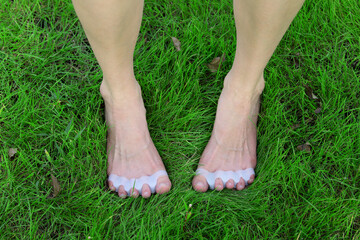 A woman's bare feet on a green grass background, wearing a silicone toe separator to promote...