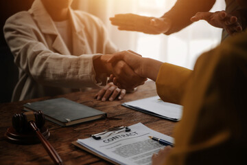 Lawyer shaking hands with a client making about documents, contracts, agreements, cooperation agreements with a female client at the lawyer's desk and a hammer at the table.