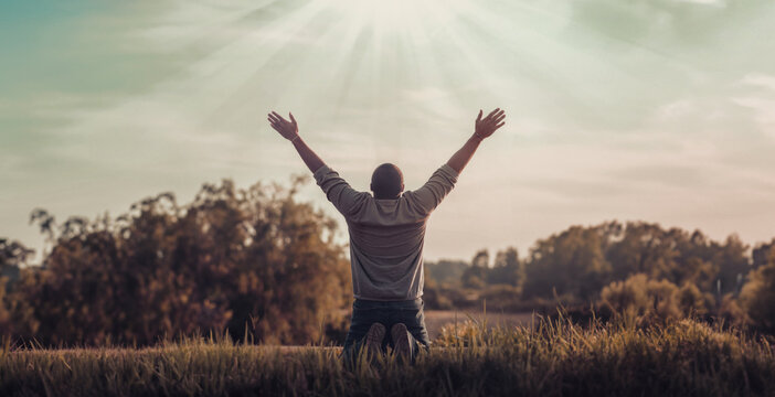 Praising the lord. Back view of a man with his arms raised to the sky in thankfulness and prayer. Themes such as Reverence, Awe, Serenity, Humility, Redemption, Resurrection, Bliss, Reflection