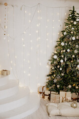 A large Christmas tree in the living room, decorated with garlands and light balloons. Bright Christmas interior with a white staircase