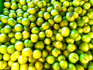 Fresh green plums piled abundantly in a market showcasing local produce under bright lighting