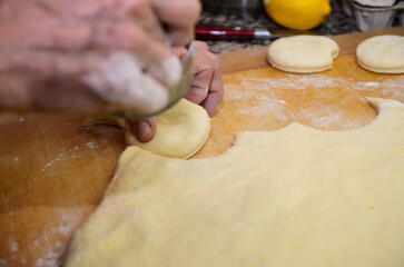 Old woman making holes in raw homemade doughnuts pastry on the kitchen table, traditional