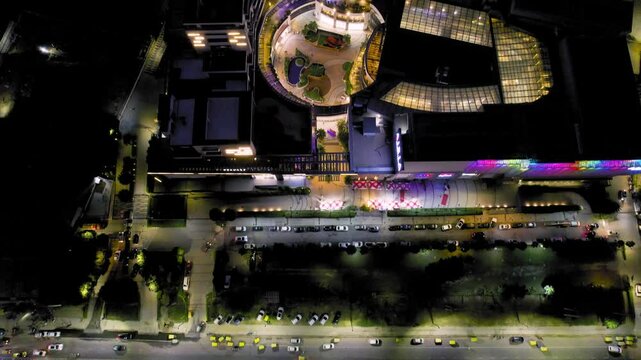 aerial drone shot straight down looking at traffic filled street, colorful mall building with open courtyard and skylight glass roof lights on the roof