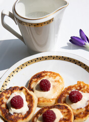 A delightful breakfast setting featuring a white ceramic pitcher with gold trim, filled with frothy milk, alongside a plate of golden pancakes