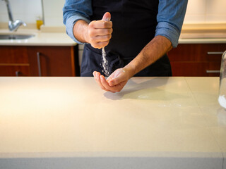 Young man putting flour on his hands before starting to knead a dough