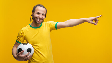 Portrait of young happy Brazilian football player or supporter posing in studio holding soocer ball...