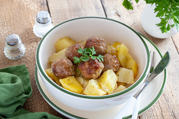 Potatoes with meatballs in a bowl on a wooden table, selective focus