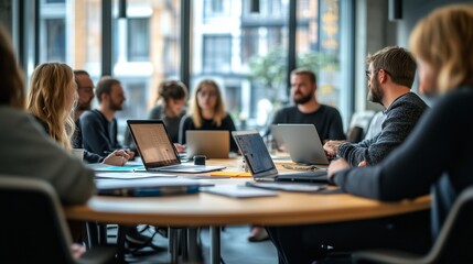 Group of professionals engaged in a collaborative meeting around a table with laptops in a modern office setting