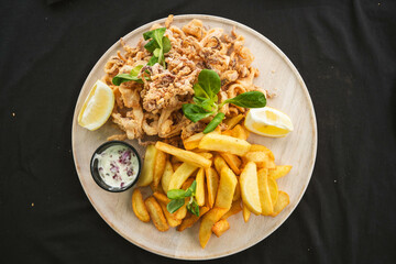 A plate of golden fried calamari rings, served with a side of dipping sauce. The crispy batter contrasts with the tender calamari inside.