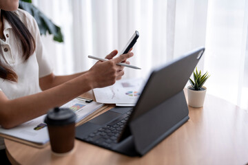 Fototapeta premium Businesswoman analyzing financial charts and using smartphone at work
