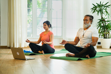 Indian couple joins online yoga on laptop at home, sitting on yoga mat together