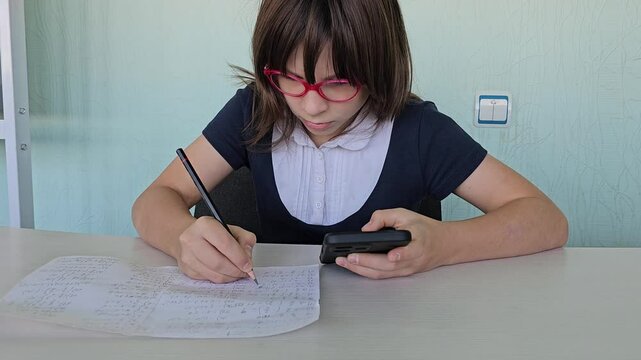 Serious kid doing classwork using smartphone in class and mobile education. Exam cheat sheet