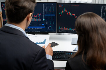 Two business traders discussing on dynamic stock market in currency rate investment trading on two pc screens with compare real time graph on risk or profit point of data at modern office. Postulate.