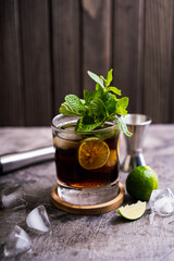 Cold Cuba Libre or Long island iced tea cocktail with brown rum, cola, mint, lime, muddler, jigger and glass