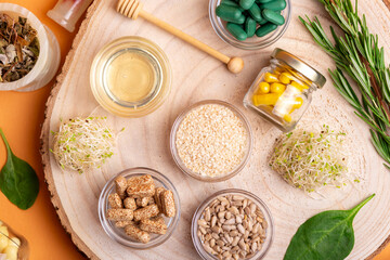 Homeopathy. Homeopathic medicine, pills and capsules in a beautiful composition with green leaves and various plants on a wooden desk on an orange background, top view