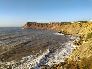 Coastal cliff view of rough waves crashing against the rocks in the afternoon sunlight at a scenic seaside location