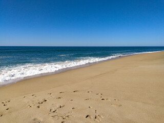 A serene beach at midday with gentle waves lapping the shore and clear blue skies inviting relaxation