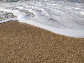 A serene beach at midday with gentle waves lapping the shore and clear blue skies inviting relaxation