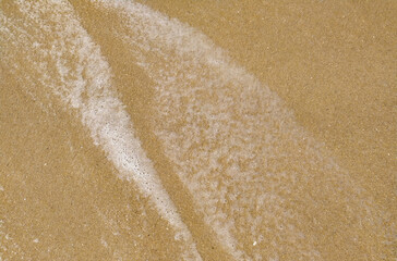 Gentle waves rolling onto sandy beach at sunrise, creating bubbles and a shimmering surface