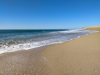 A serene beach at midday with gentle waves lapping the shore and clear blue skies inviting relaxation