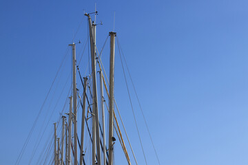 Masts of small yachts against the blue sky. Many yacht masts against the bright sky. Sports and recreation