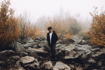 Man Standing On Rocky Terrain In Foggy Autumn Forest.