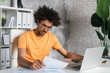 Portrait of concentrated young casually dressed entrepreneur or business analyst working on laptop in modern light colored office interior