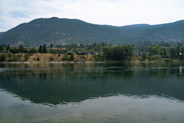 Serene river landscape with reflections of mountains and trees in the soft light of a summer afternoon near a quiet residential area