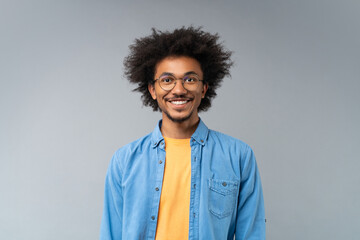 Studio portrait of smiling handsome African American young man in spectacles posing over grey background