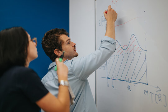 Two students actively engage in a classroom setting, discussing and analyzing data visualizations on a whiteboard. They are focused and involved in a collaborative learning experience.