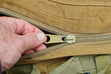 fingers of hand zipping plastic zipper on dirty yellow military fashionable nylon stylish men army...